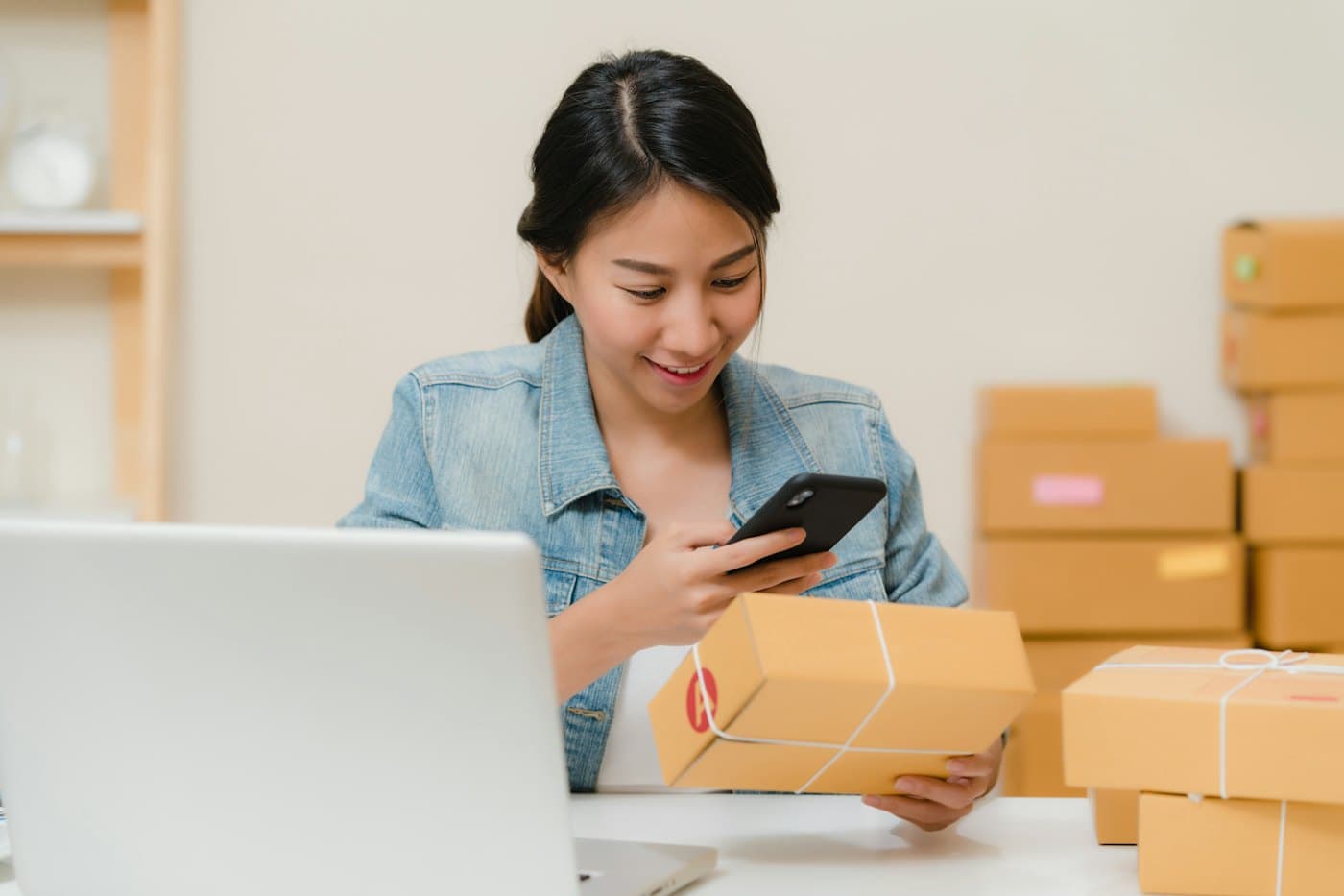 A business owner checking an order on her phone, surrounded by packed boxes