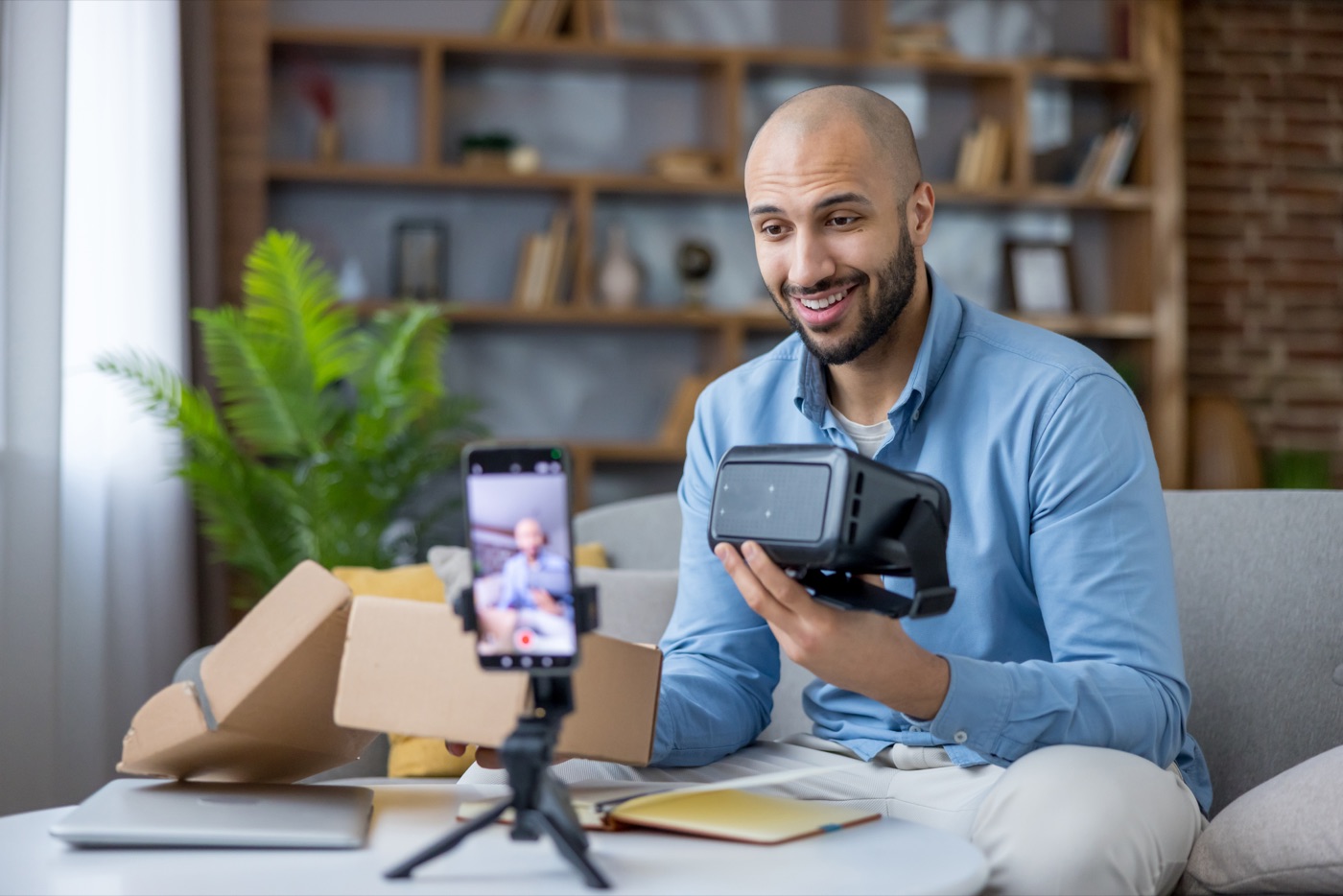 A man unboxing a VR headset in front of his phone while filming a product review